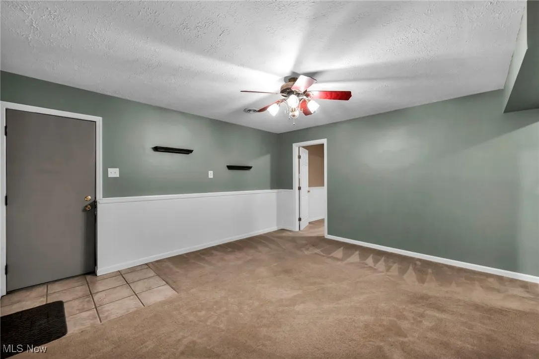 Carpeted spare room with a ceiling fan, a textured ceiling, a wainscoted wall, and tile patterned floors