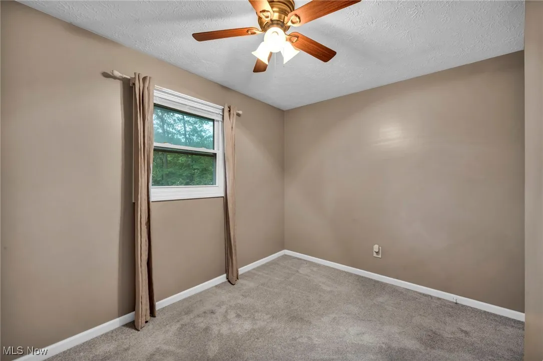 Spare room featuring a textured ceiling, light colored carpet, and a ceiling fan