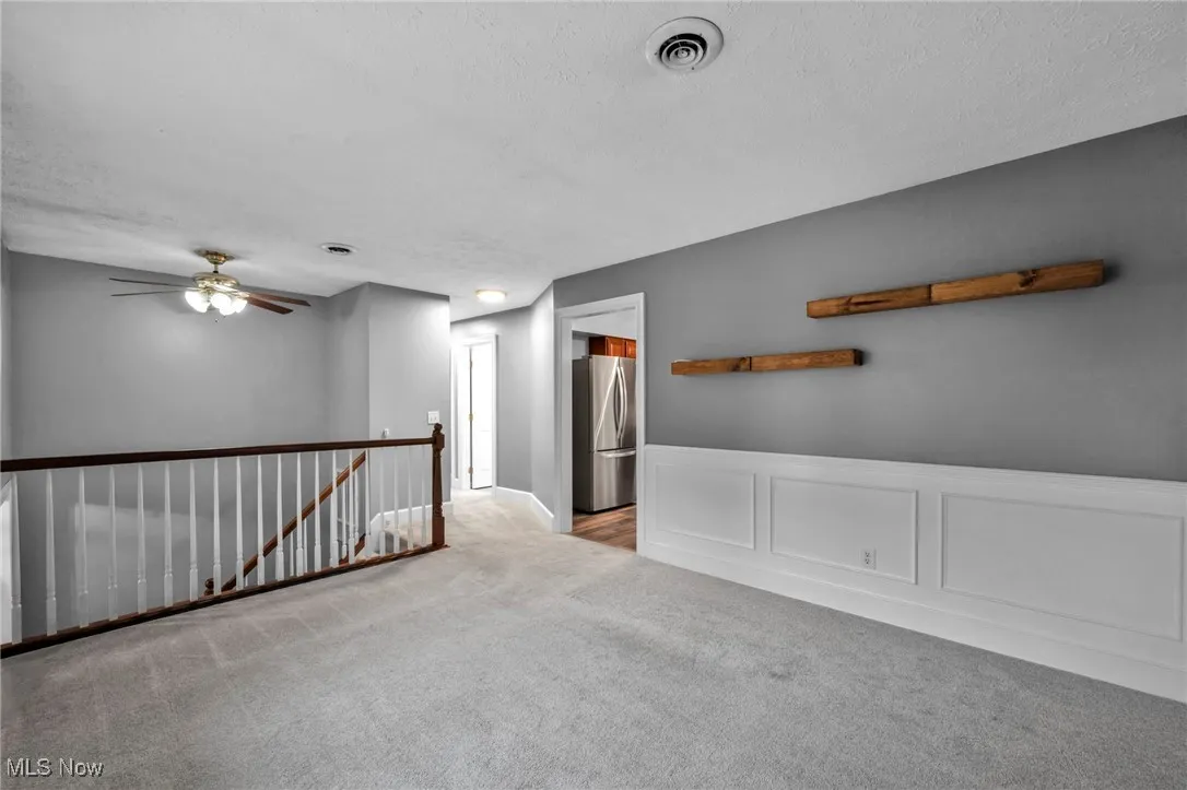Empty room featuring a decorative wall, carpet, a wainscoted wall, a textured ceiling, and ceiling fan