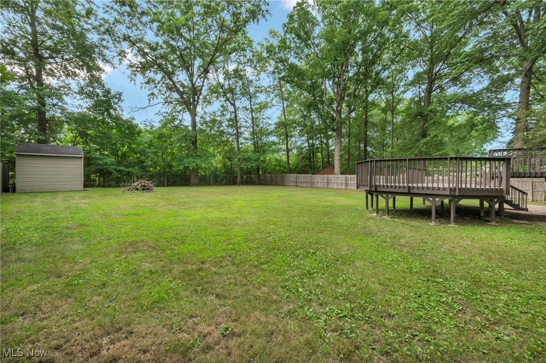 Fenced backyard featuring a wooden deck, a shed, and stairs