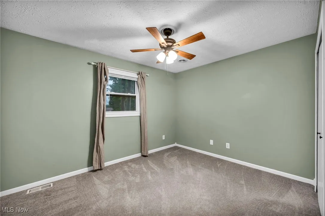 Empty room with ceiling fan, carpet, and a textured ceiling