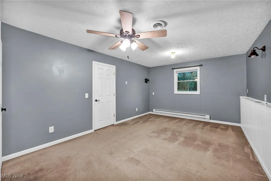 Carpeted spare room with a textured ceiling, a ceiling fan, and baseboard heating