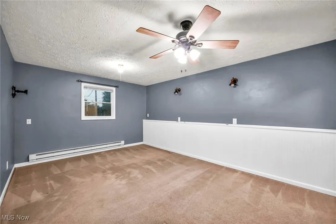 Spare room with a textured ceiling, baseboard heating, ceiling fan, carpet flooring, and a wainscoted wall