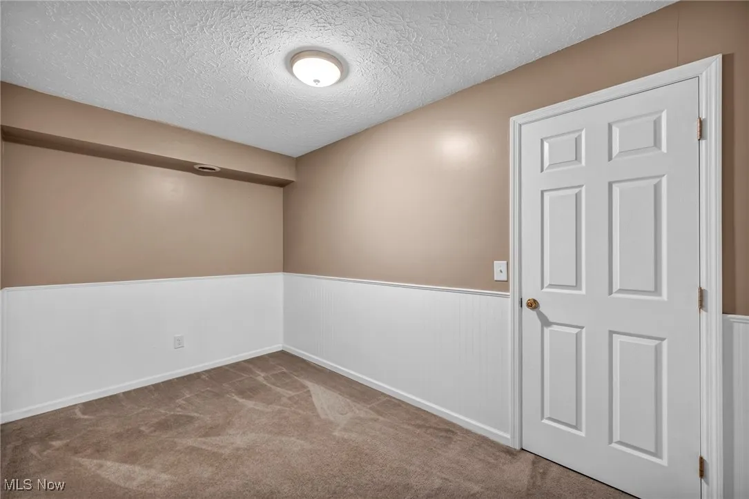 Spare room with a wainscoted wall, a textured ceiling, and carpet floors