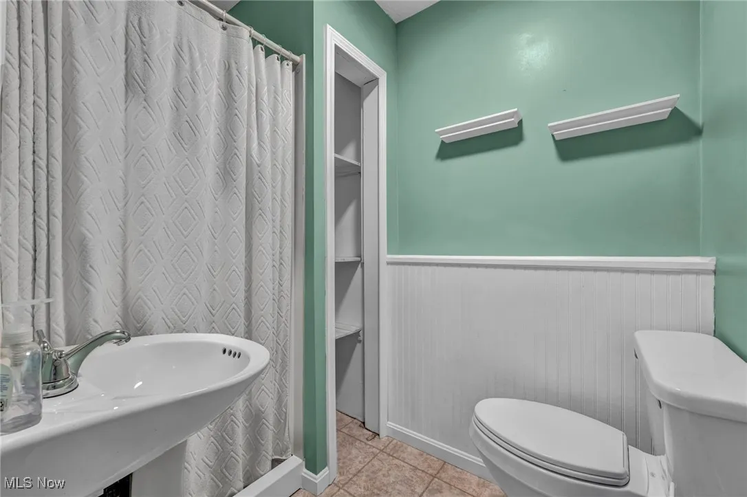 Full bath with a wainscoted wall, tile patterned floors, and curtained shower
