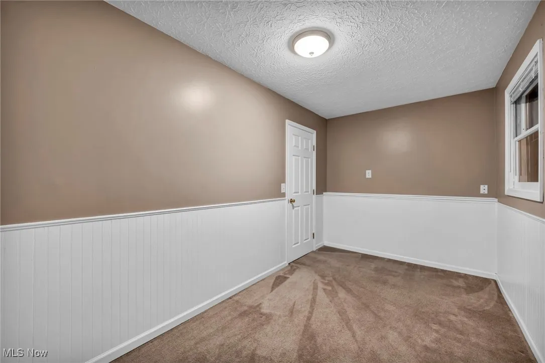 Unfurnished room featuring wainscoting, a textured ceiling, and carpet