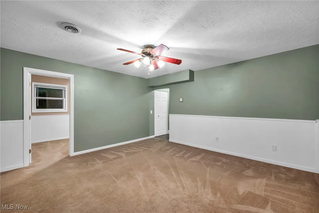 Carpeted empty room featuring ceiling fan, wainscoting, and a textured ceiling