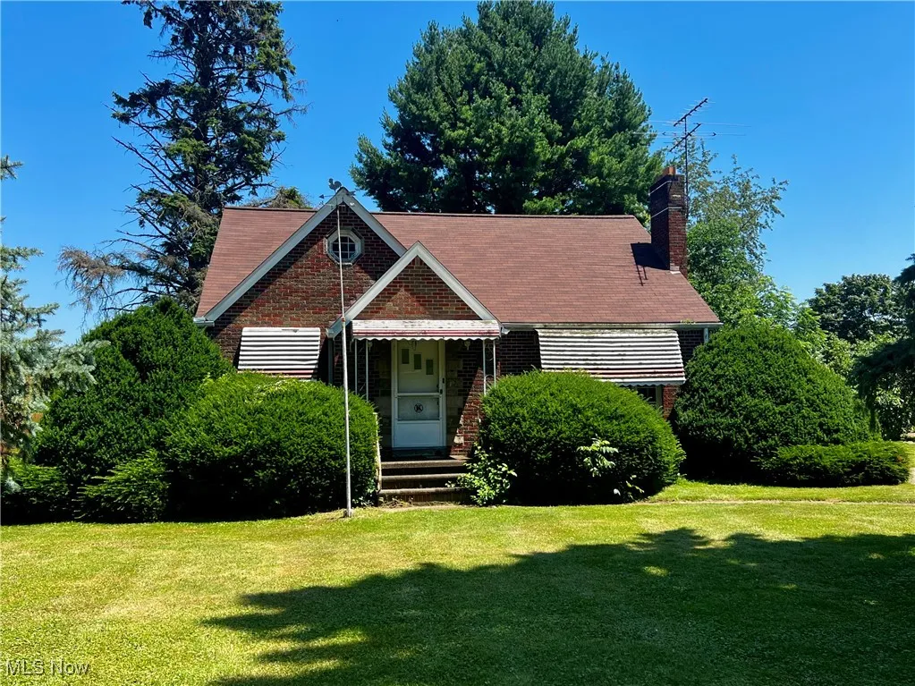 View of front of house with a front yard, a chimney, and brick siding