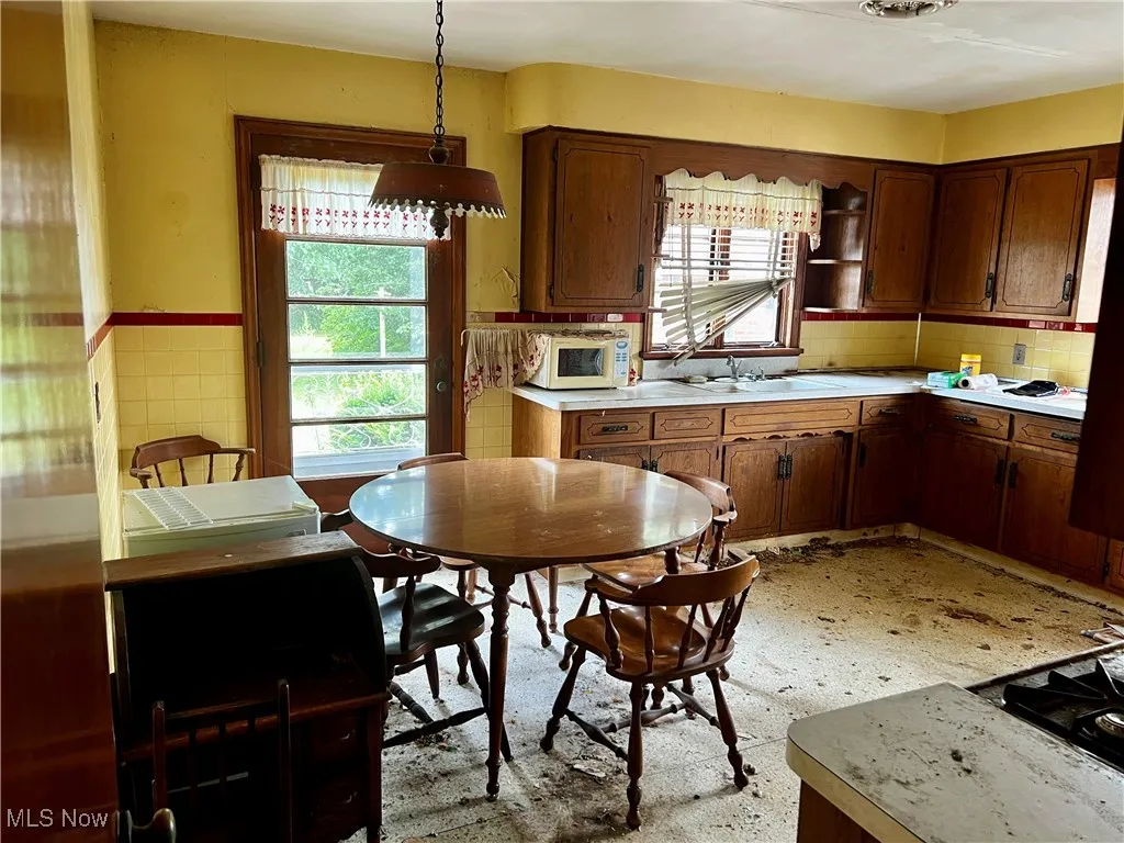 Kitchen featuring light countertops, pendant lighting, white microwave, decorative backsplash, and brown cabinetry