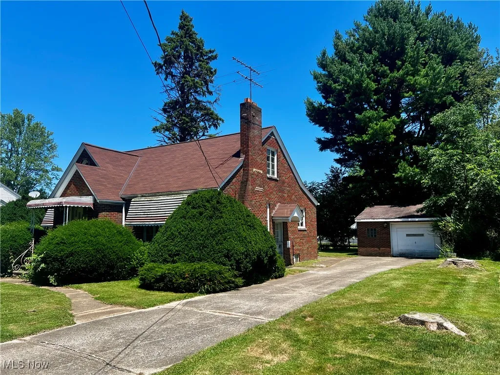 View of home's exterior featuring brick siding, a yard, a chimney, driveway and garage