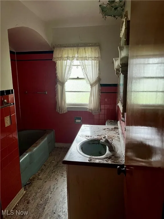 Bathroom with a tub to relax in, vanity, a wainscoted wall, and tile walls