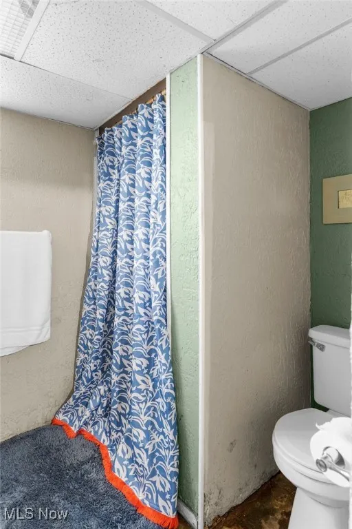 Bathroom with a textured wall, a paneled ceiling, and curtained shower