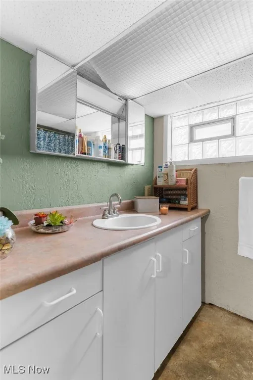 Bathroom with a textured wall, concrete floors, and vanity