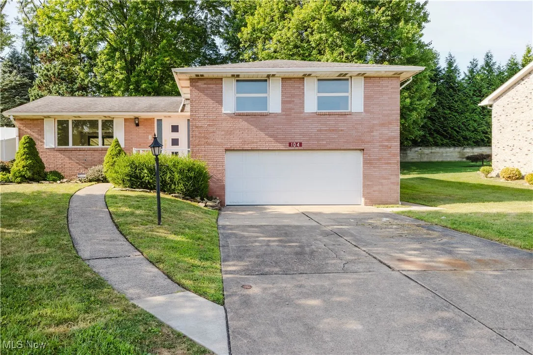 Split level home featuring brick siding, driveway, an attached garage, and a front yard