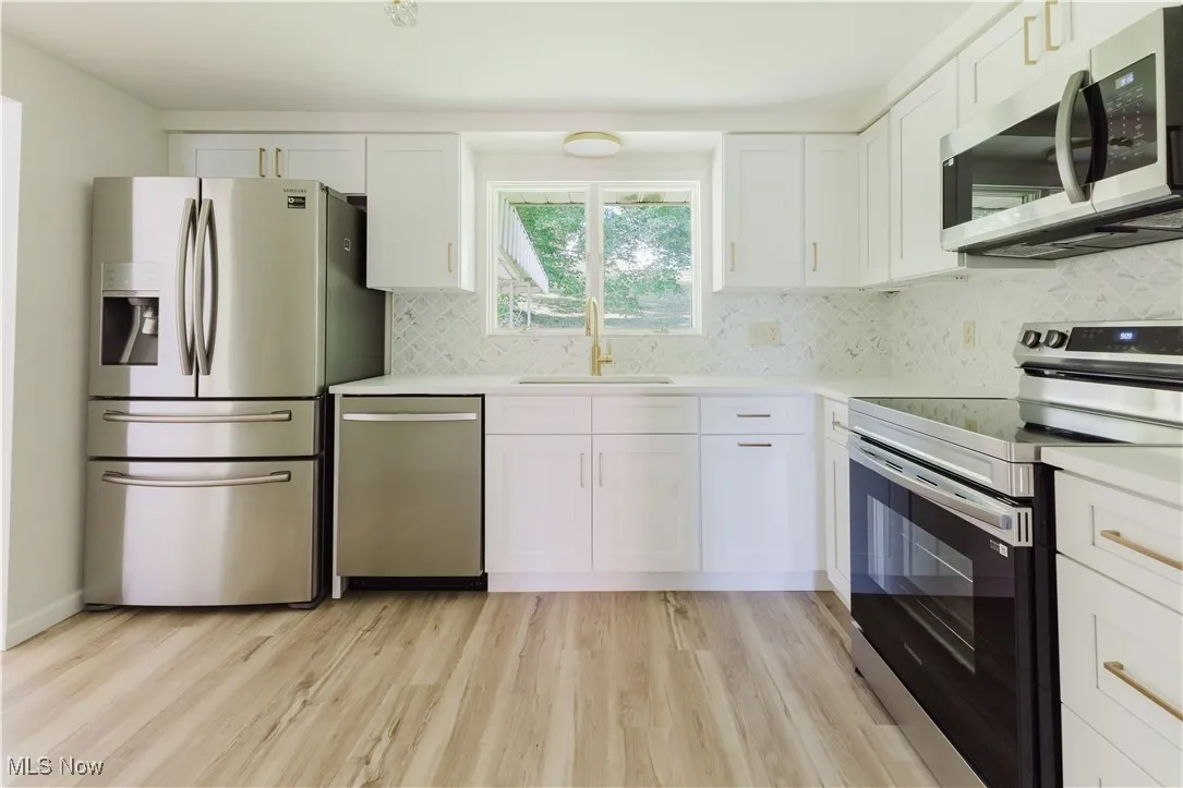 Kitchen featuring appliances with stainless steel finishes, light countertops, white cabinetry, light wood finished floors, and tasteful backsplash