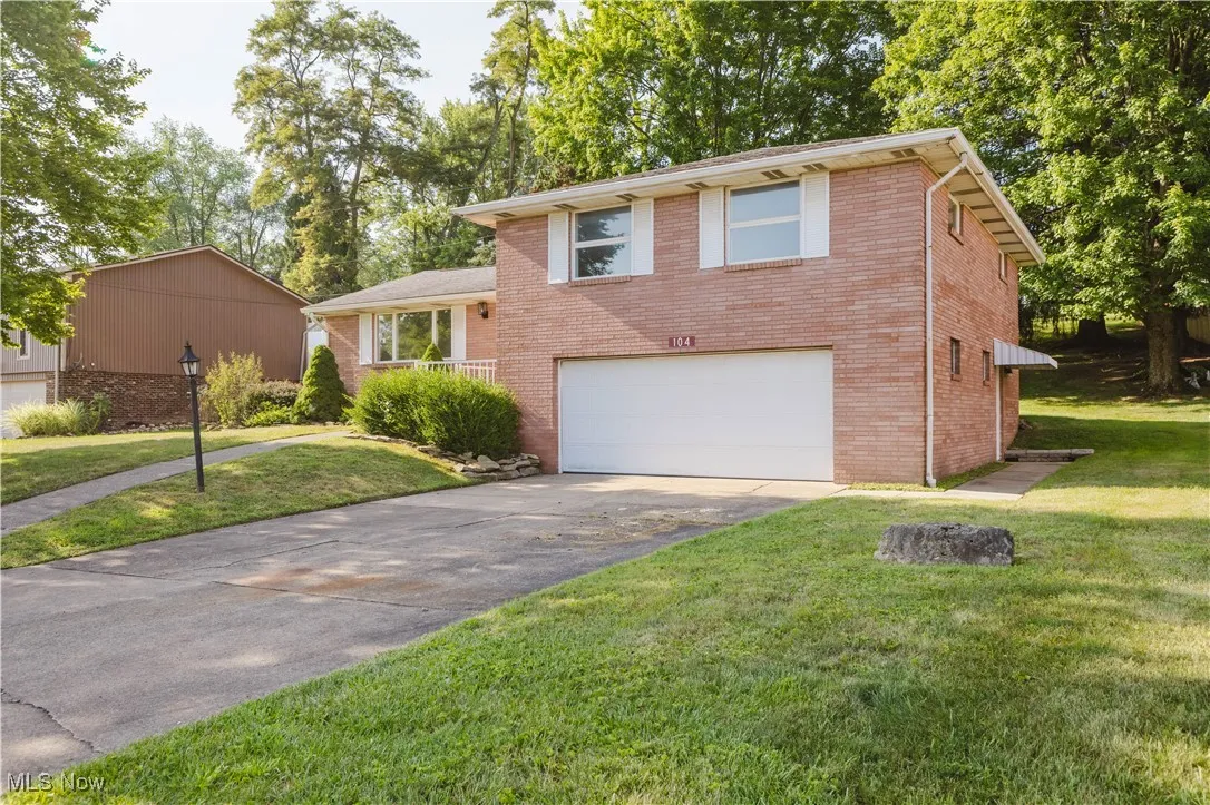 Tri-level home featuring driveway, brick siding, an attached garage, and a front yard