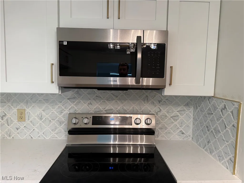 Kitchen view of appliances with stainless steel finishes, light countertops, white cabinetry, and decorative backsplash