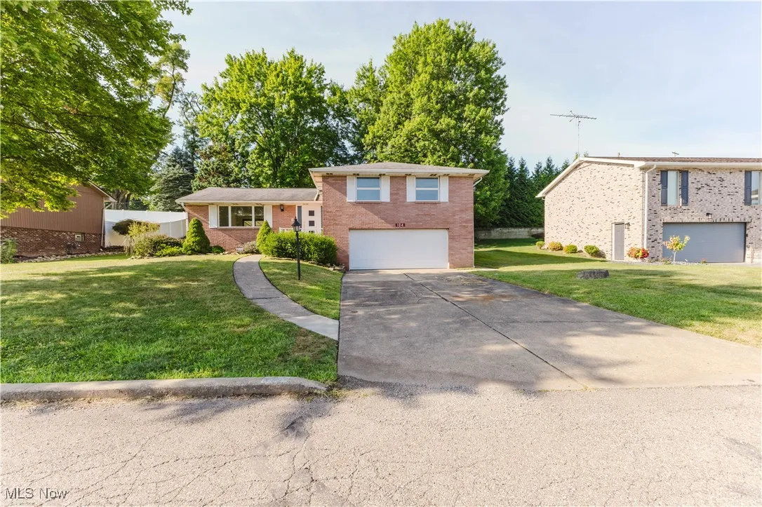Tri-level home with an attached garage, brick siding, concrete driveway, and a front lawn