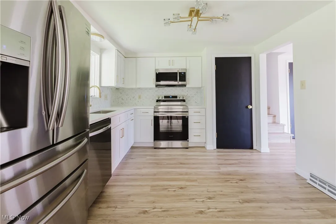 Kitchen with stainless steel appliances, backsplash, light wood-style flooring, light countertops, and white cabinetry