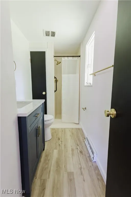 Bathroom featuring vanity, a baseboard heating unit, wood finished floors, and a shower with shower curtain