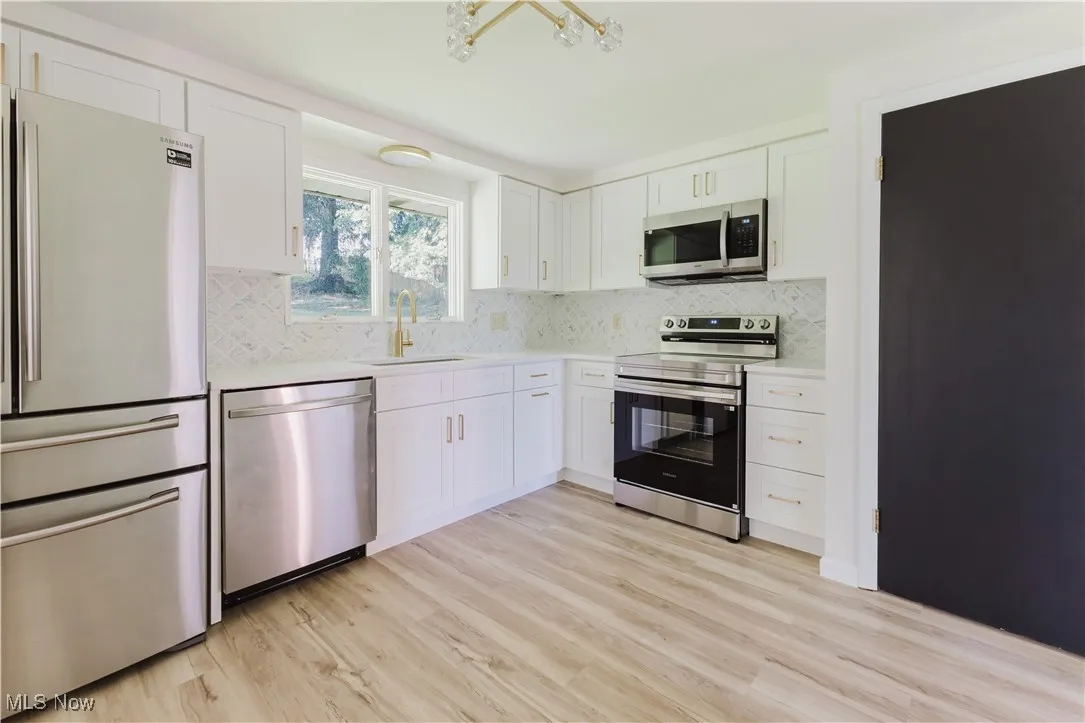 Kitchen featuring appliances with stainless steel finishes, light countertops, white cabinetry, and light wood-type flooring
