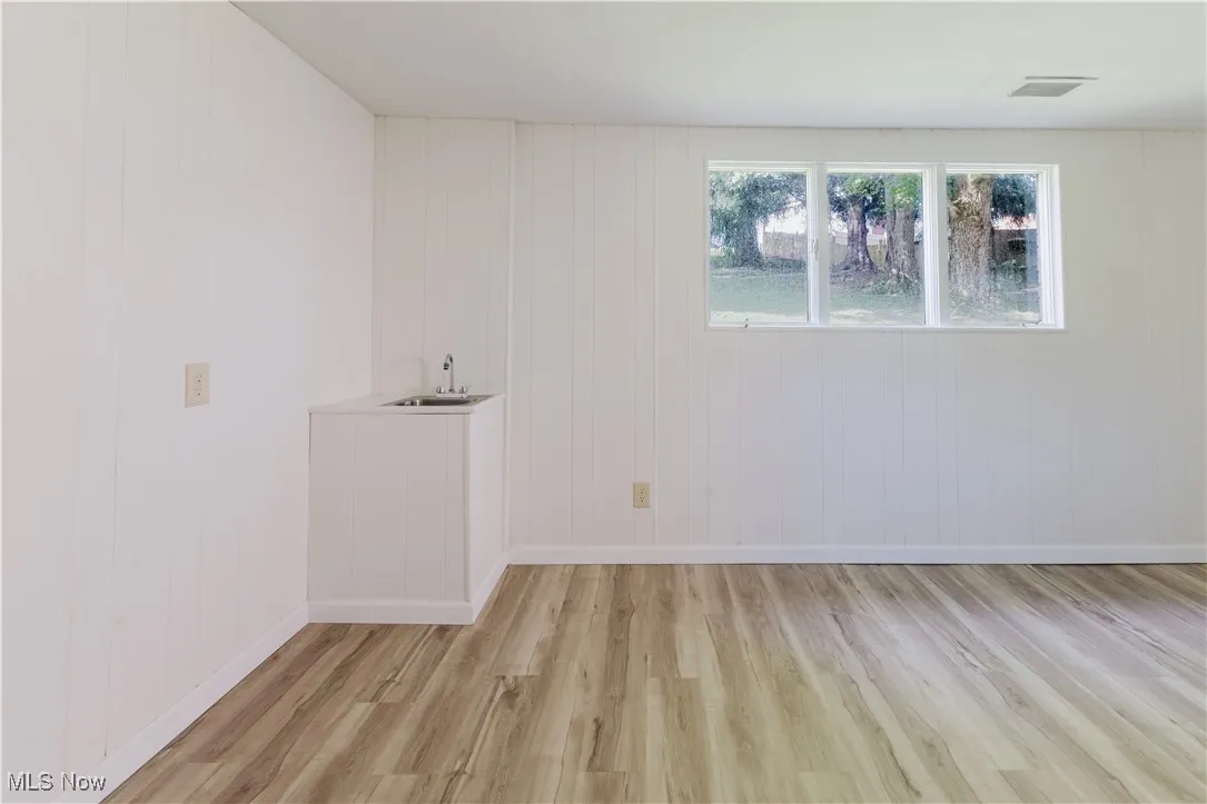 Unfurnished room featuring light wood-type flooring, wood walls, and bar with sink