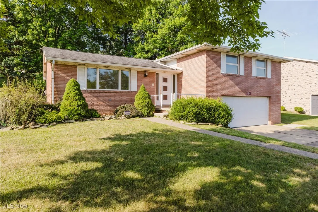 Tri-level home with brick siding, a garage, concrete driveway, and a front lawn