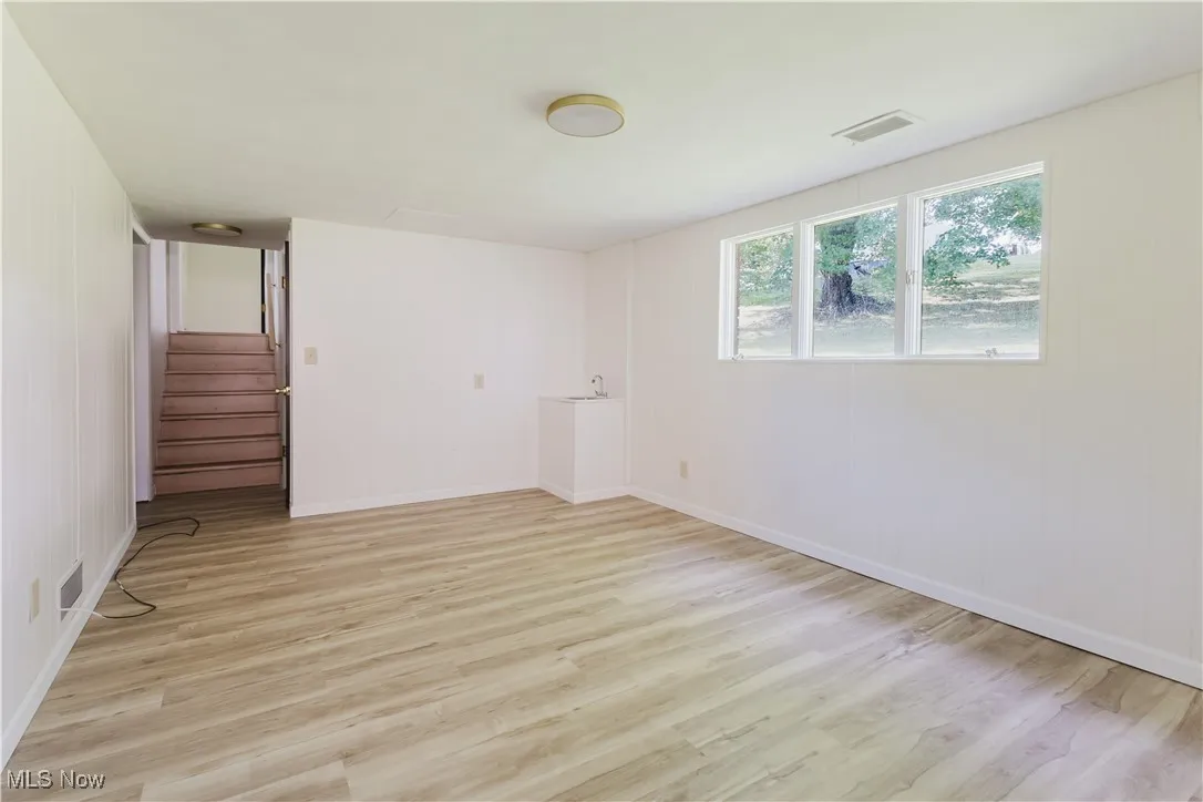 Unfurnished room featuring light wood-style floors, stairs, and wooden walls
