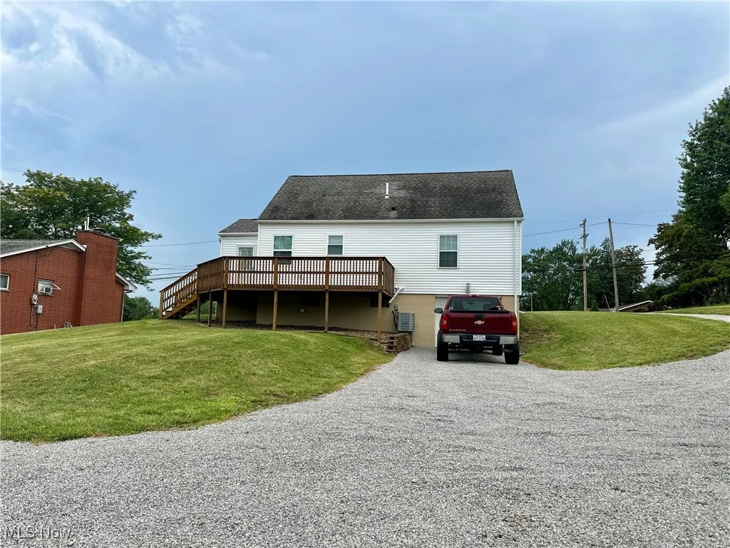 Back of property with driveway, a deck, a yard, and stairway