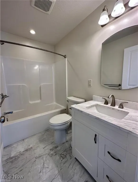 Bathroom with a textured ceiling, vanity, tub / shower combination, marble finish floors, and recessed lighting
