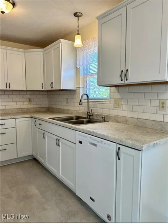 Kitchen featuring white dishwasher, light countertops, decorative light fixtures, white cabinetry, and tasteful backsplash