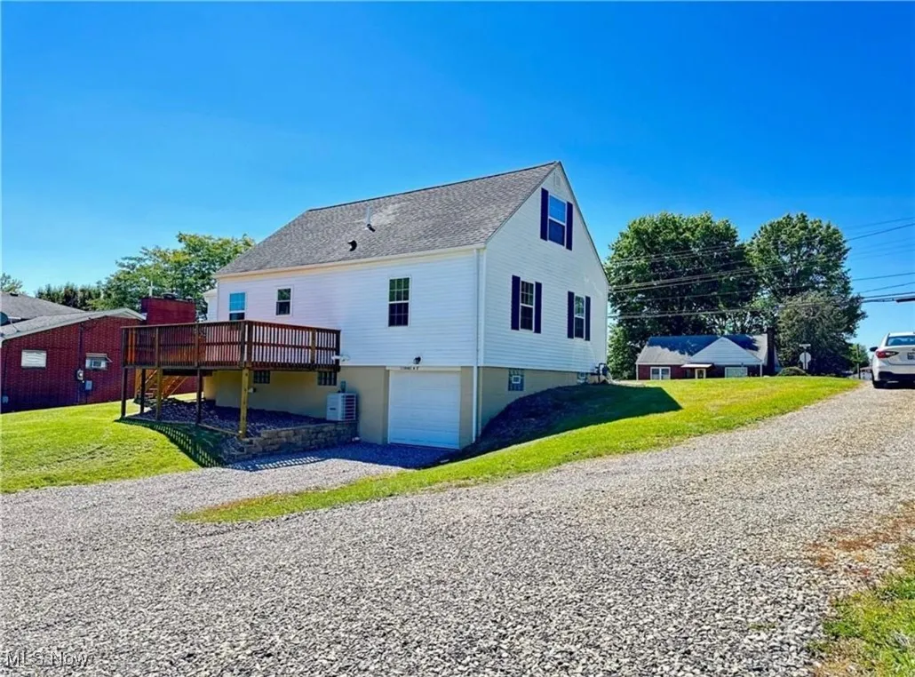 View of side of home featuring a garage, a deck, gravel driveway, and a yard