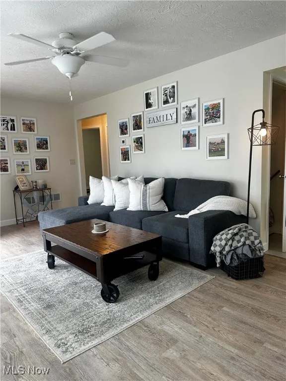 Living room with a textured ceiling, wood finished floors, and ceiling fan