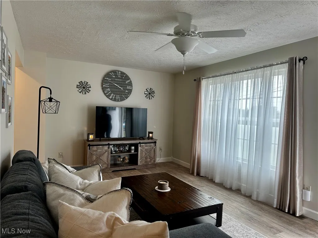 Living area featuring light wood-style floors, a textured ceiling, and a ceiling fan