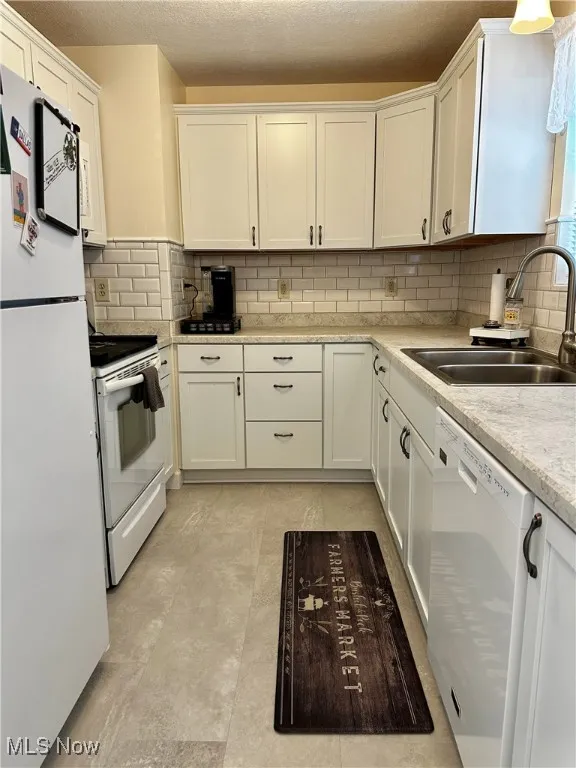 Kitchen featuring white appliances, white cabinets, light countertops, tasteful backsplash, and a textured ceiling
