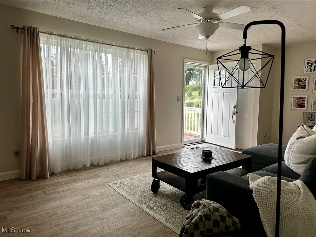 Living area featuring a textured ceiling, light wood finished floors, and ceiling fan