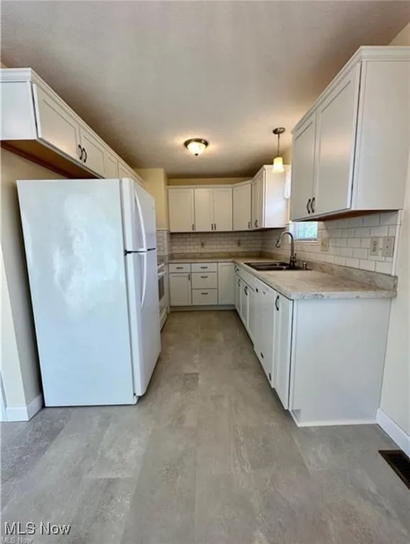 Kitchen featuring white appliances, light countertops, tasteful backsplash, white cabinets, and decorative light fixtures