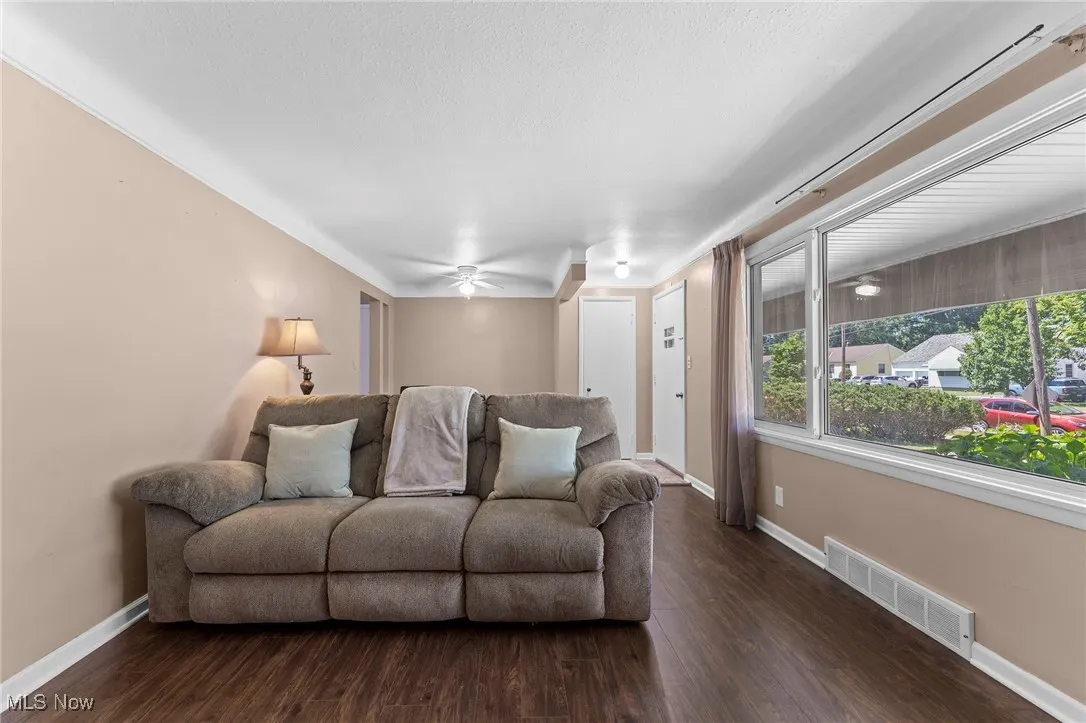 Living room with dark wood like flooring, a ceiling fan, and ornamental molding