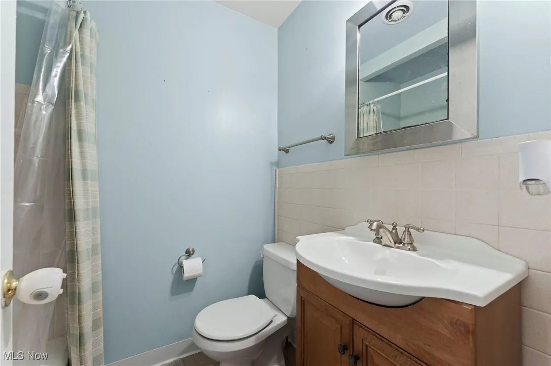 Full bath featuring tile walls, vanity, a shower with shower curtain, and wainscoting