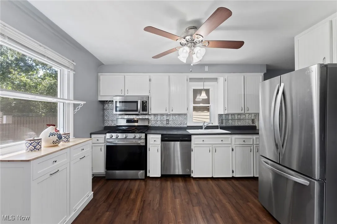 Kitchen with appliances with stainless steel finishes, tasteful backsplash, dark wood-style floors, and white cabinets