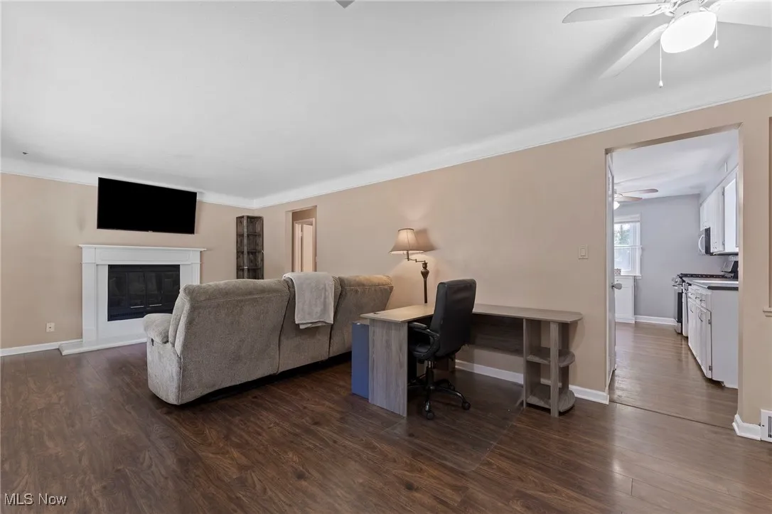 Living room featuring ceiling fan, dark wood-type flooring, ornamental molding, and a glass covered fireplace