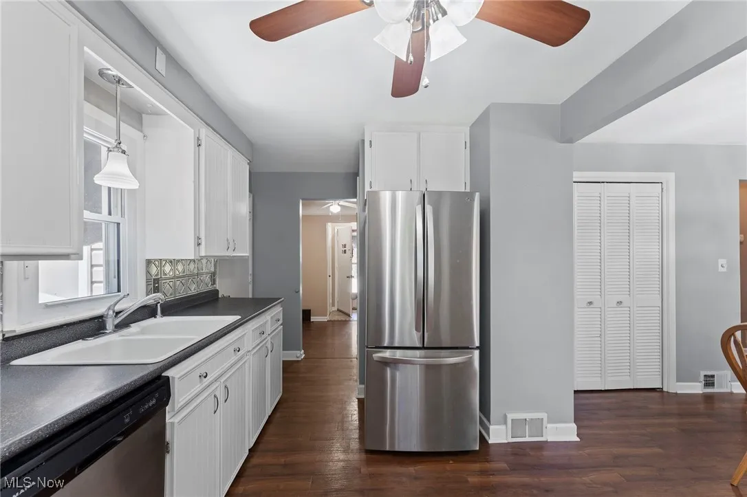 Kitchen featuring ceiling fan, stainless steel appliances, dark countertops, and dark wood like flooring