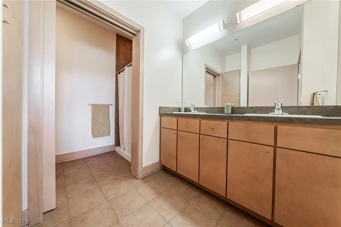 Full bathroom featuring double vanity, a walk-in shower, storage, and tile flooring.