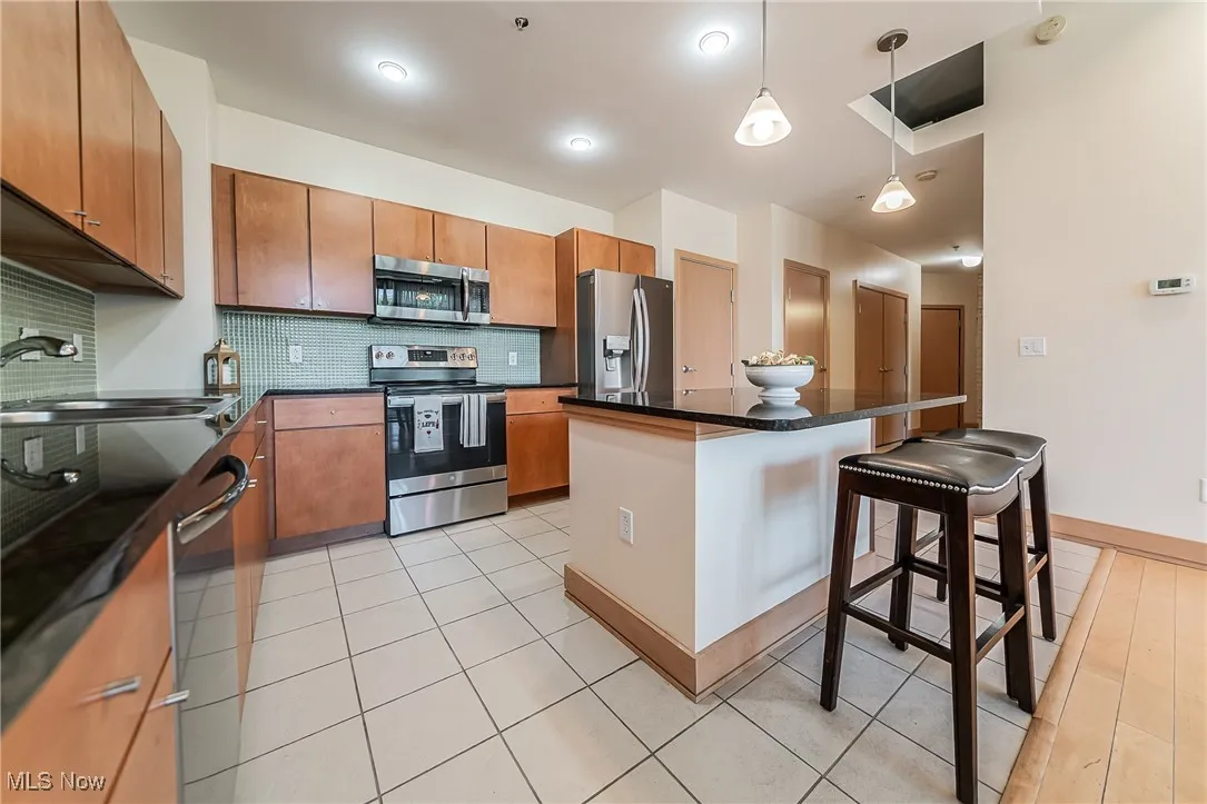Kitchen with stainless steel appliances, tasteful backsplash, a kitchen breakfast bar, dark countertops, and  pendant lights.