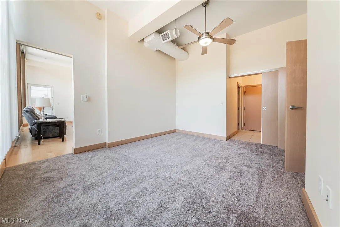 Bedroom featuring high ceiling, light carpet, walk-in closet, ceiling fan, and bathroom access.