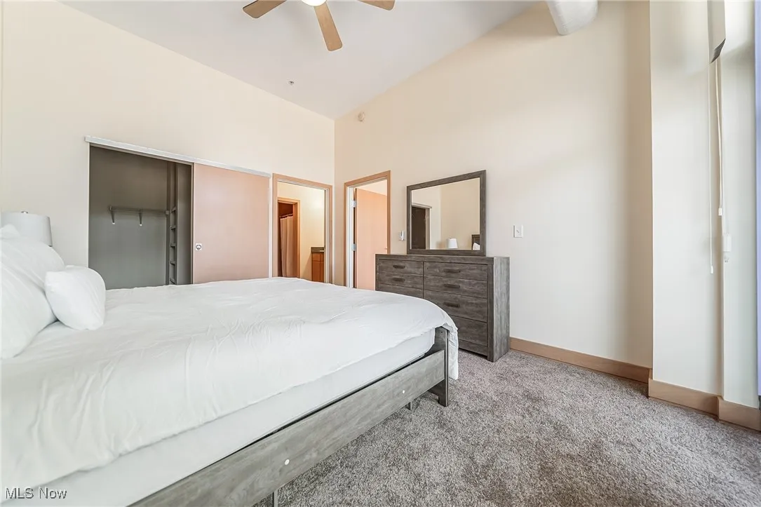 Carpeted bedroom with ceiling fan, balcony access, walk-in closet, and full bathroom.