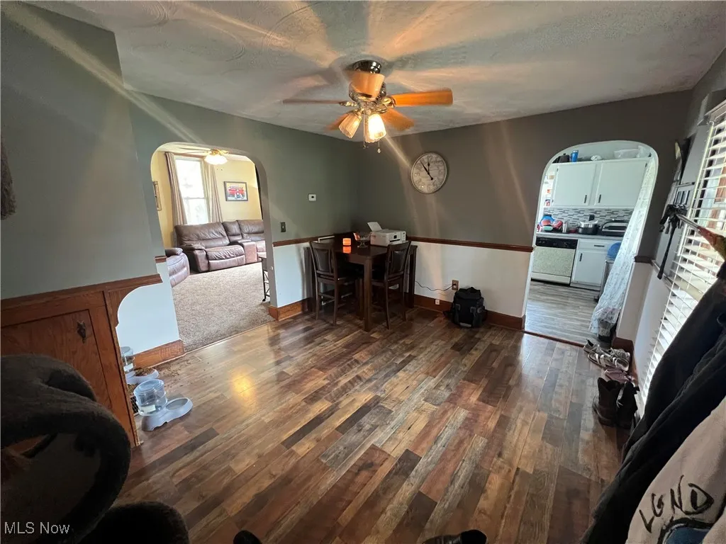 Office featuring arched walkways, ceiling fan, dark wood-style floors, a textured ceiling, and wainscoting