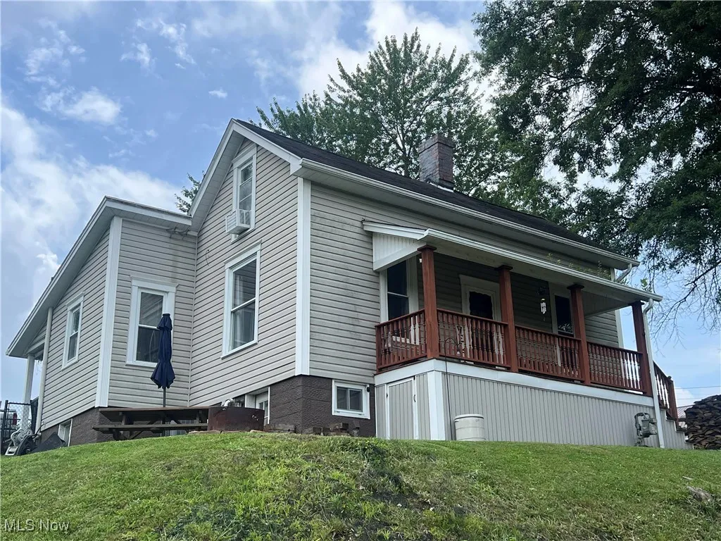 View of side of property featuring a chimney, a lawn, and covered porch