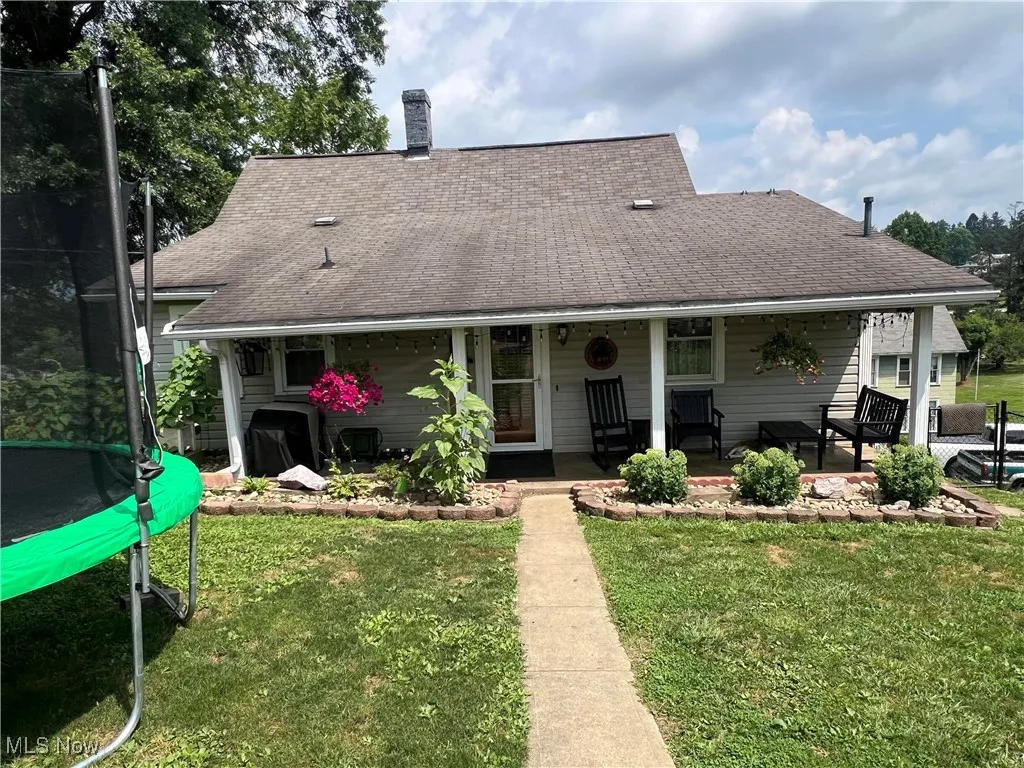 Rear view of house featuring a trampoline, a lawn, and a shingled roof
