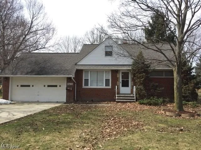 Bungalow-style home with brick siding, entry steps, an attached garage, and driveway